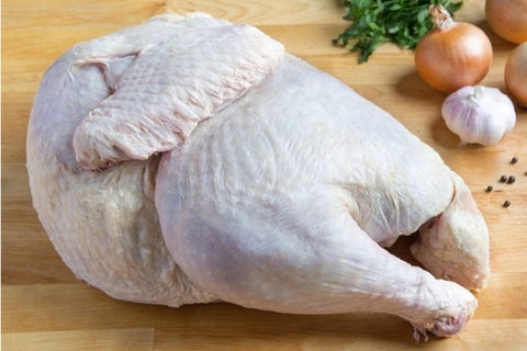 Raw whole chicken on a wooden surface with onions and garlic