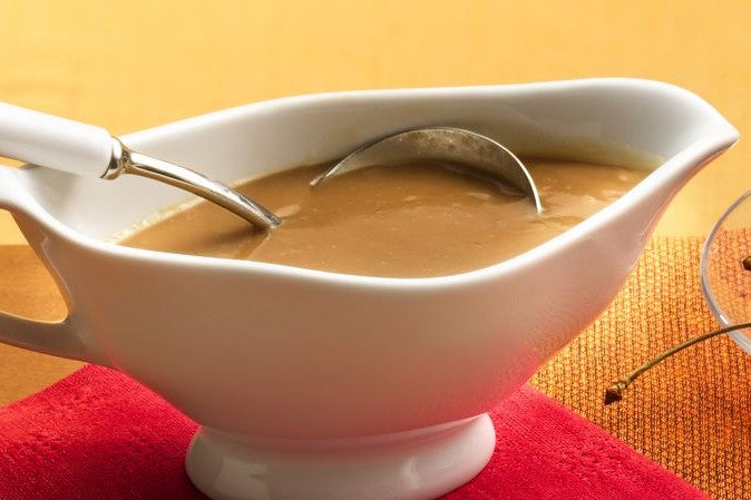 White gravy boat filled with brown sauce and a spoon resting inside
