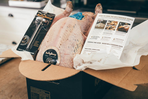 A raw turkey inside a cardboard box with cooking instructions and a meat thermometer.