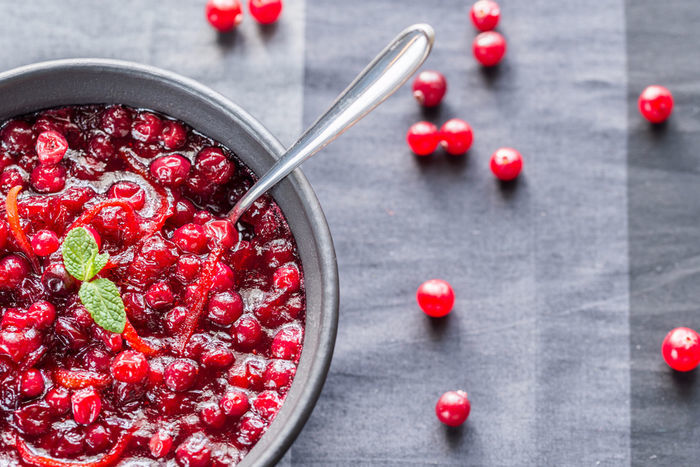 A bowl of cranberry sauce garnished with mint leaves, surrounded by scattered cranberries.