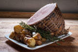 A platter featuring a sliced ham with roasted potatoes and sprigs of thyme.